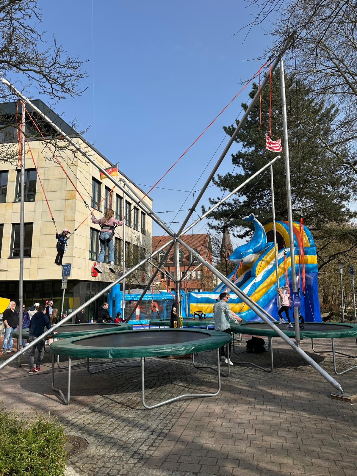 Kinder springen an der 4er-Bungee-Trampolinanlage von Galaxy Jump, im Hintergrund die Hüpfburg-Kombination